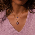 Woman wearing an Ombre Peridot Flower Necklace and a gold chain with purple pendants, paired with a soft purple V-neck sweater.