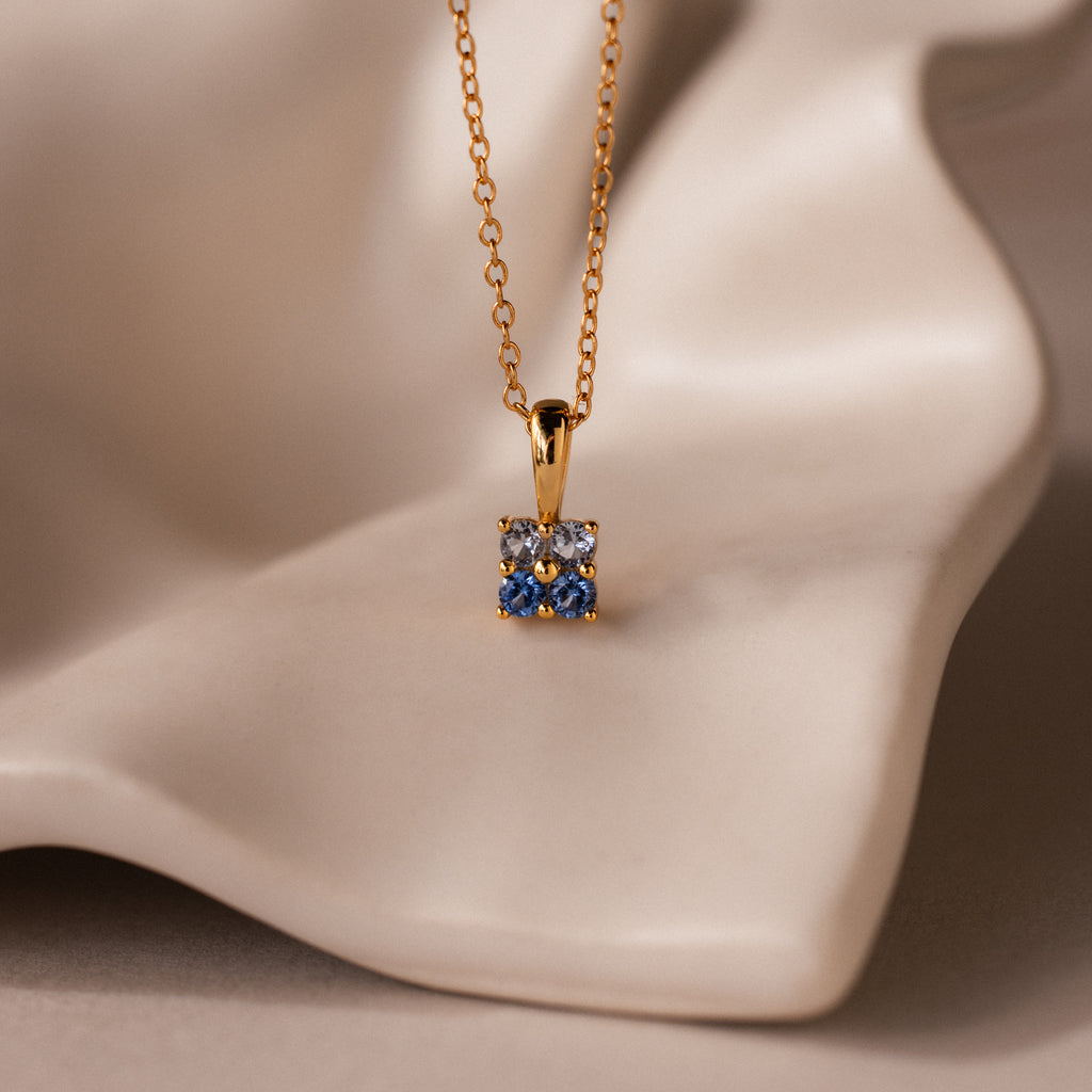 Ombre Aquamarine Flower Necklace featuring a square blue and white pendant, elegantly displayed on a smooth, cream-colored surface.