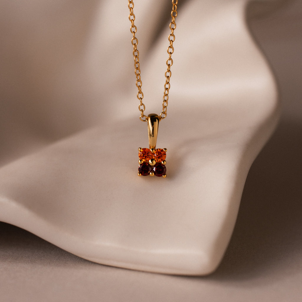 Ombre Garnet Flower Necklace with a delicate pendant featuring two orange gemstones, displayed on a soft beige surface.