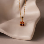 Ombre Garnet Flower Necklace with a delicate pendant featuring two orange gemstones, displayed on a soft beige surface.