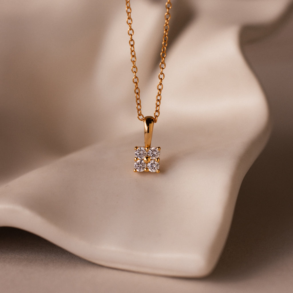 The Ombre Diamond Flower Necklace features a gold chain and a cluster-inspired pendant, displayed on smooth beige fabric.