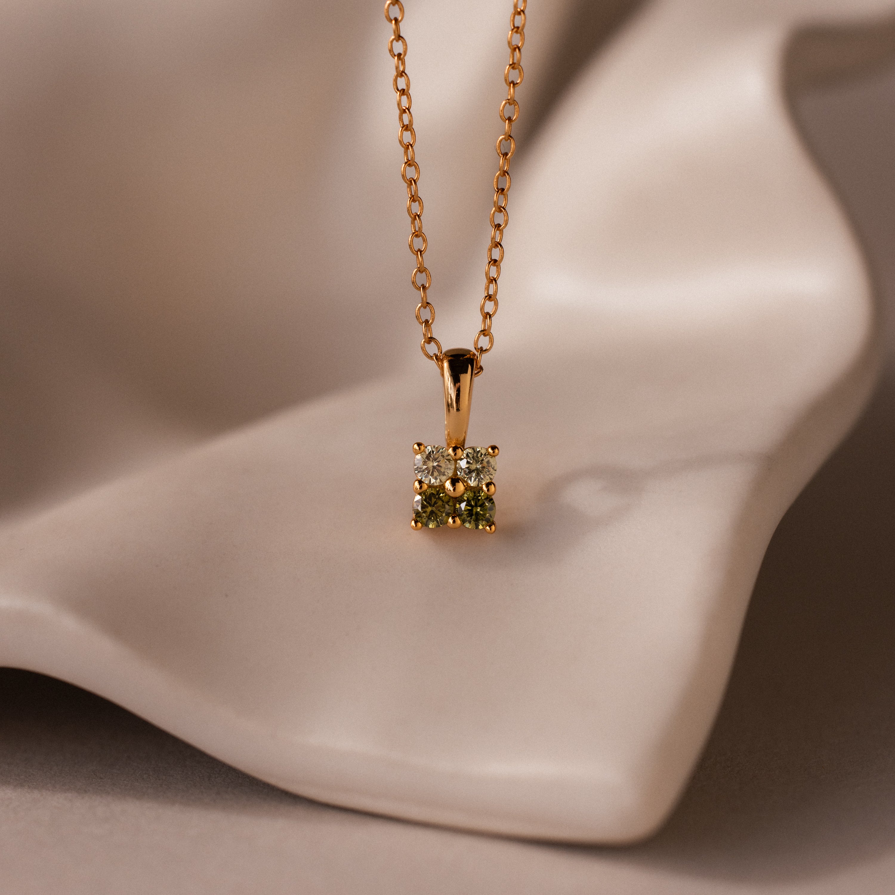 Ombre Peridot Flower Necklace with a gold chain and floral pendant, reminiscent of a Gradient Gemstone Necklace, displayed on a smooth, cream-colored surface.