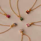 Six Ombre Sapphire Flower Necklaces are arranged in a circle on a beige surface, showcasing their vibrant gradient sapphire pendants.