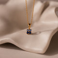 Ombre Blue Zircon Flower Necklace featuring a square blue gemstone pendant displayed on soft, wavy beige fabric—ideal for those who love elegant birthstone jewelry.