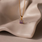 Ombre Alexandrite Flower Necklace highlighted by a delicate purple gemstone pendant, beautifully showcased on a soft, beige draped surface.