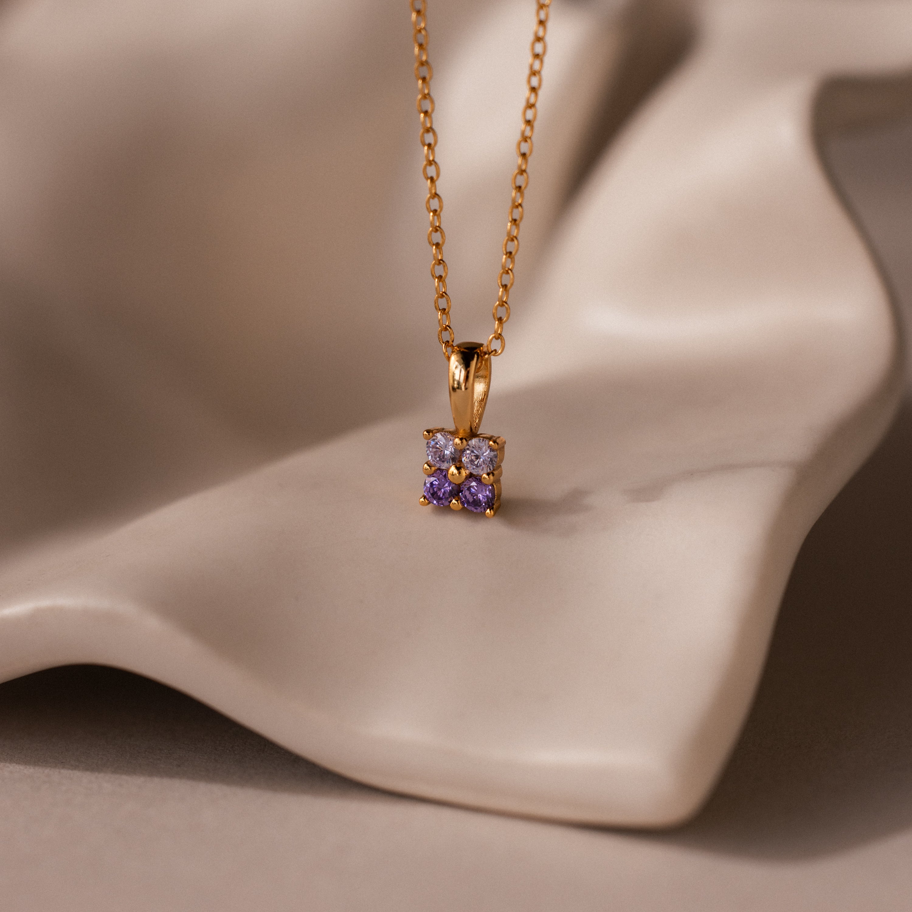 Ombre Alexandrite Flower Necklace highlighted by a delicate purple gemstone pendant, beautifully showcased on a soft, beige draped surface.