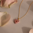 The Ruby Crystal Necklace features a heart-shaped pink jewel, bezel set like a birthstone, and adorned with pale rose petals.