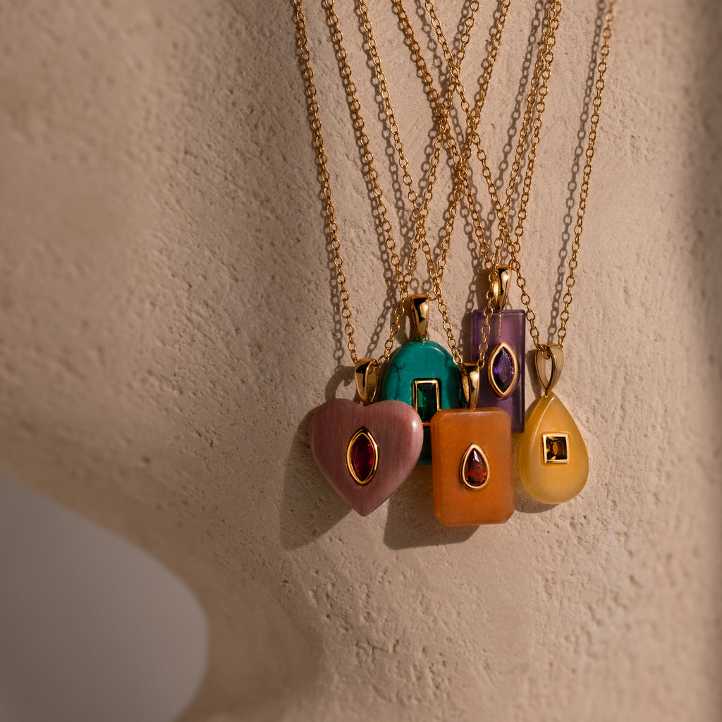 Five Amethyst Crystal Necklaces with gold chains and gemstone pendants display elegant birthstone jewelry against a beige surface.
