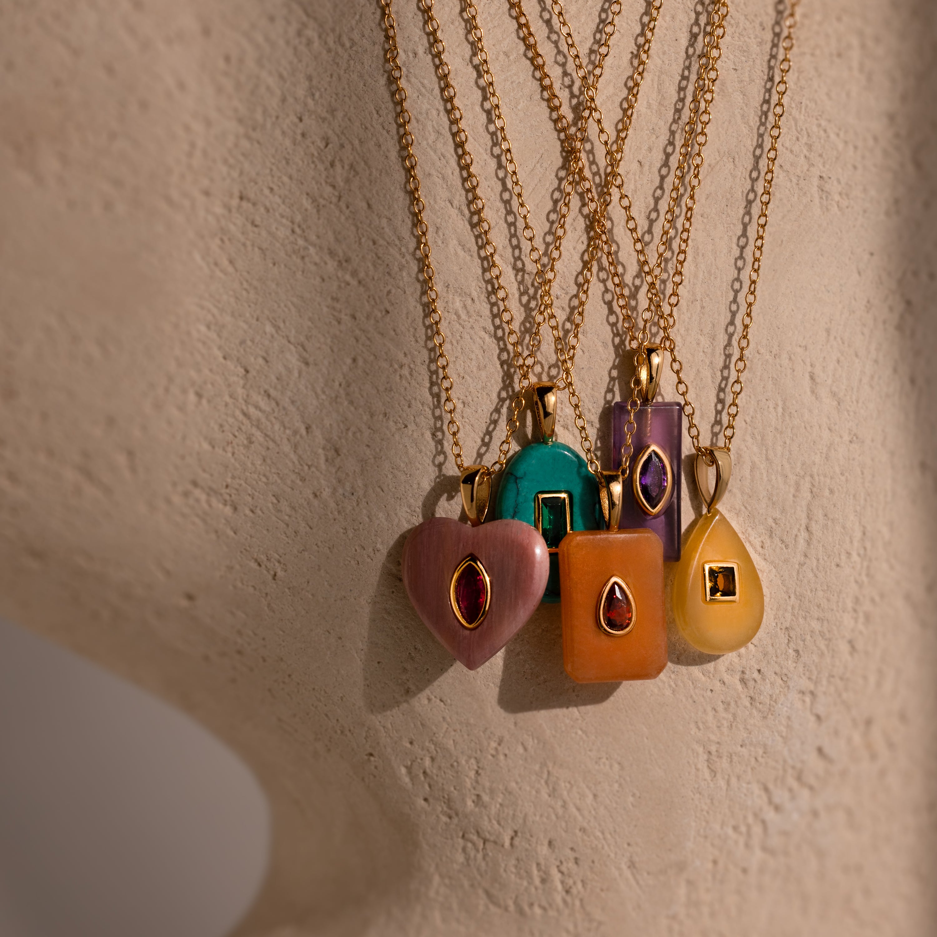 Five Amethyst Crystal Necklaces with gold chains and gemstone pendants display elegant birthstone jewelry against a beige surface.