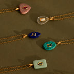 Five Ruby Crystal Necklaces with bezel-set gemstones and colorful shapes arranged on a vibrant green background.