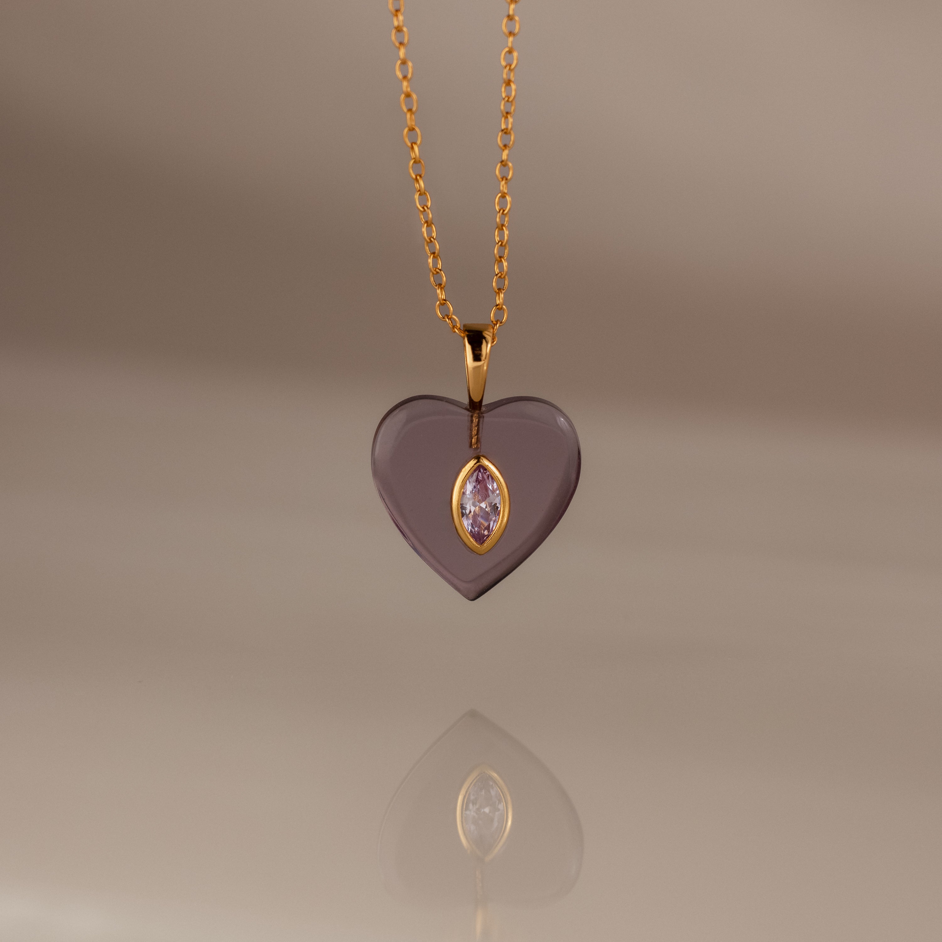 Alexandrite Crystal Necklace: A heart-shaped gold pendant with a central gem, elegantly hanging from a gold chain and showcased on a soft beige background. Perfect as birthstone jewelry or a stunning Birthstone Crystal Necklace for any occasion.