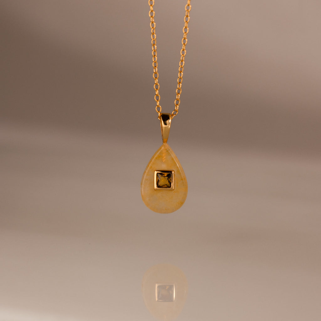 The Topaz Crystal Necklace showcases a gold teardrop pendant with a square detail on a simple gold chain—ideal for layering or wearing alone as a distinctive Birthstone Crystal Necklace.