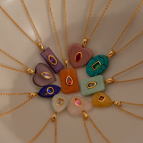 Twelve Birthstone Crystal Necklaces with gold chains are displayed in a circle on a neutral background, highlighting the colorful elegance of this birthstone jewelry.