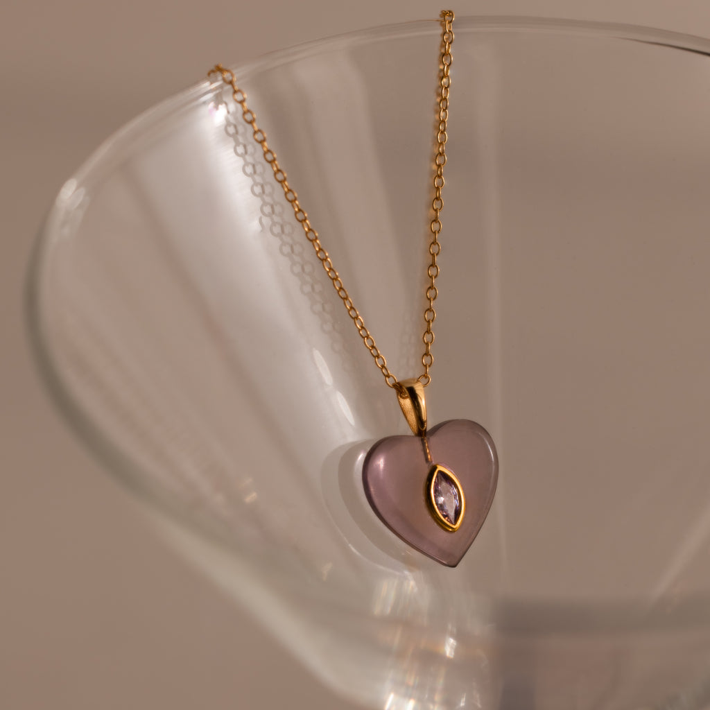 Alexandrite Crystal Necklace featuring a purple heart pendant, perfect as birthstone jewelry, displayed elegantly on the rim of a clear glass.