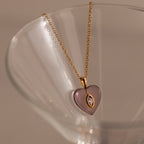 Alexandrite Crystal Necklace featuring a purple heart pendant, perfect as birthstone jewelry, displayed elegantly on the rim of a clear glass.