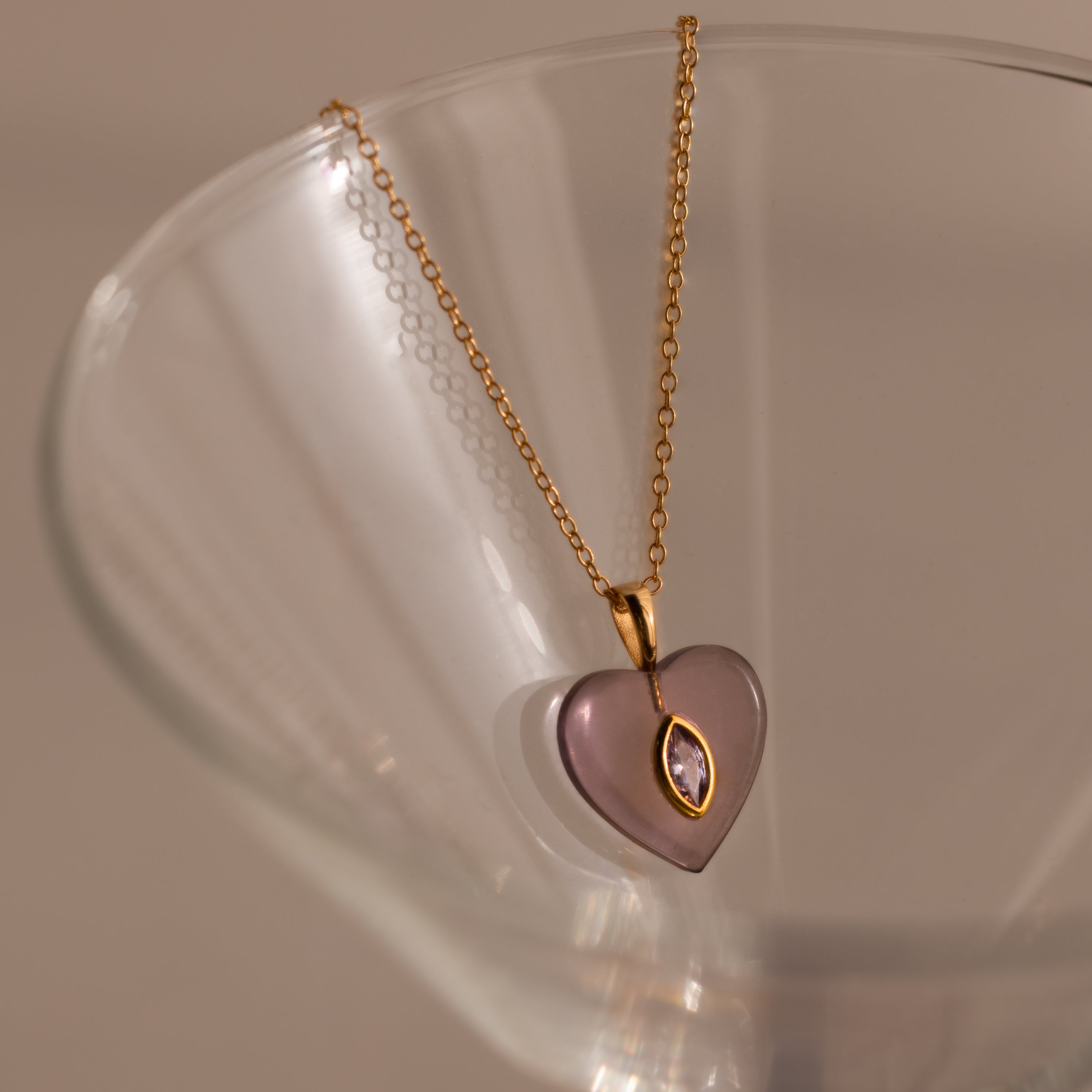 Alexandrite Crystal Necklace featuring a purple heart pendant, perfect as birthstone jewelry, displayed elegantly on the rim of a clear glass.