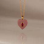 The Ruby Crystal Necklace features a gold chain with a pink heart-shaped pendant, showcasing a bezel-set ruby crystal at its center and accented in gold.