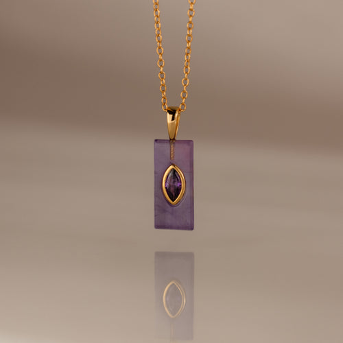 Gold chain necklace with a rectangular purple pendant and gold accent, reflected on a smooth surface—an elegant Amethyst Crystal Necklace perfect for adding a touch of birthstone jewelry to any look.