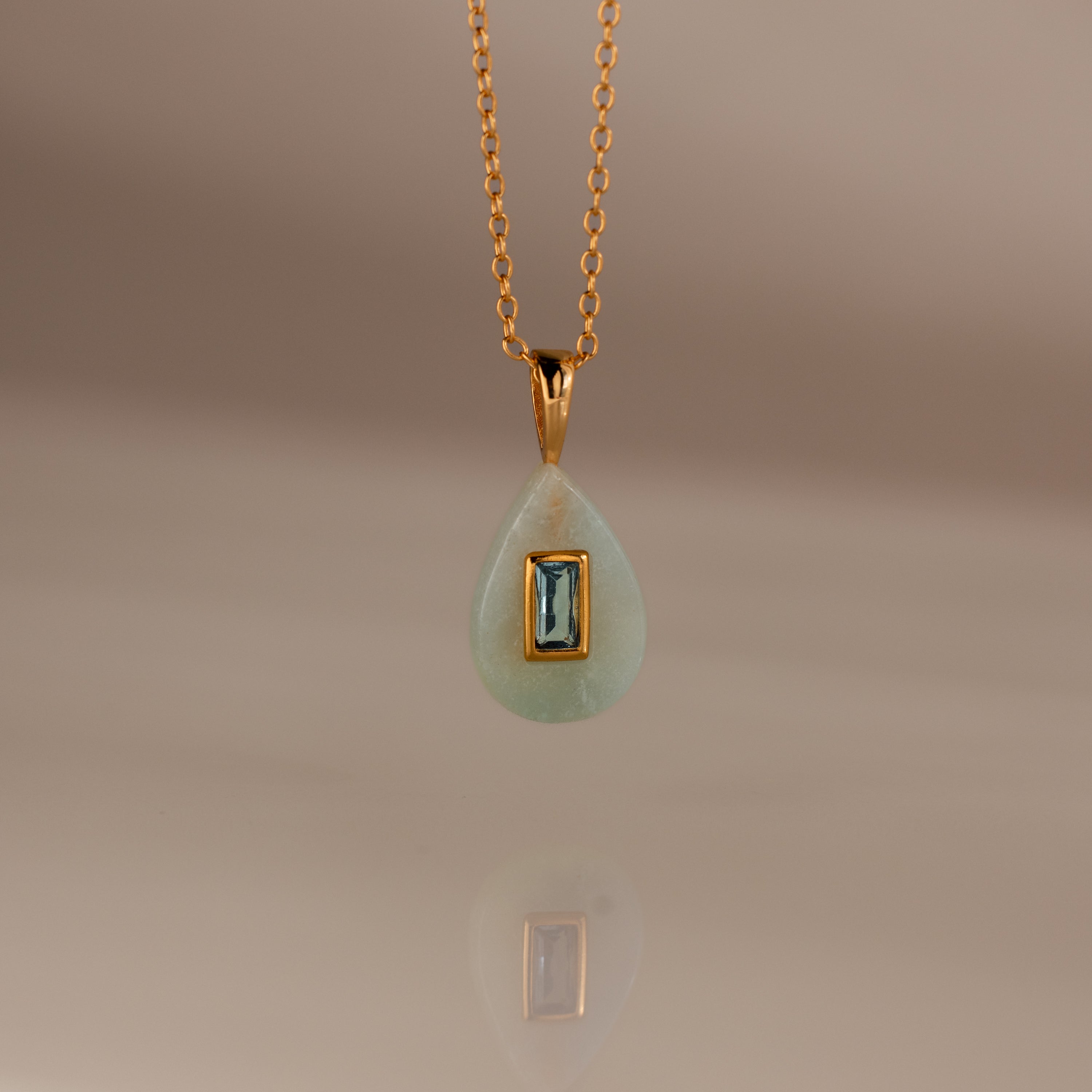 Aquamarine Crystal Necklace: Features a gold chain with a teardrop-shaped green birthstone pendant accented by a rectangular blue gemstone at the center—an eye-catching piece of jewelry.