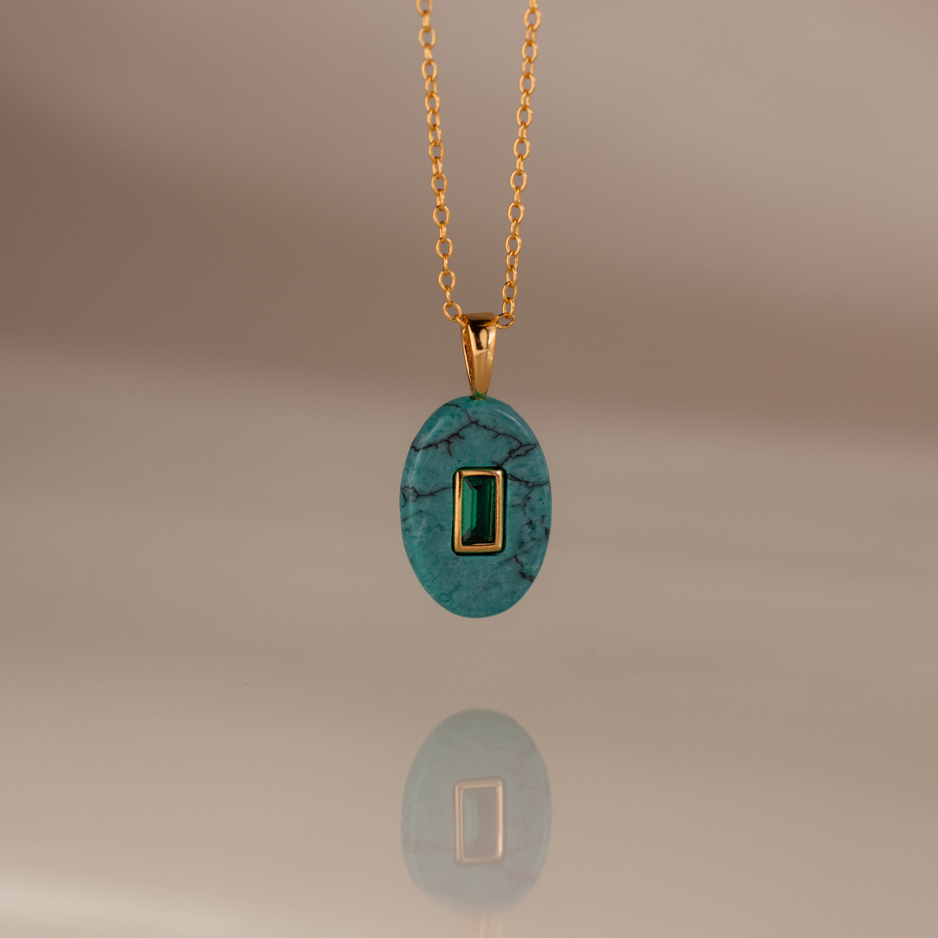 The Emerald Crystal Necklace features an oval turquoise pendant with a rectangular green gemstone at its center—a stunning birthstone jewelry piece.