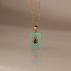 The Peridot Crystal Necklace features a rectangular green crystal pendant in a gold bezel setting, highlighted by a gold-trimmed teardrop accent at the center.