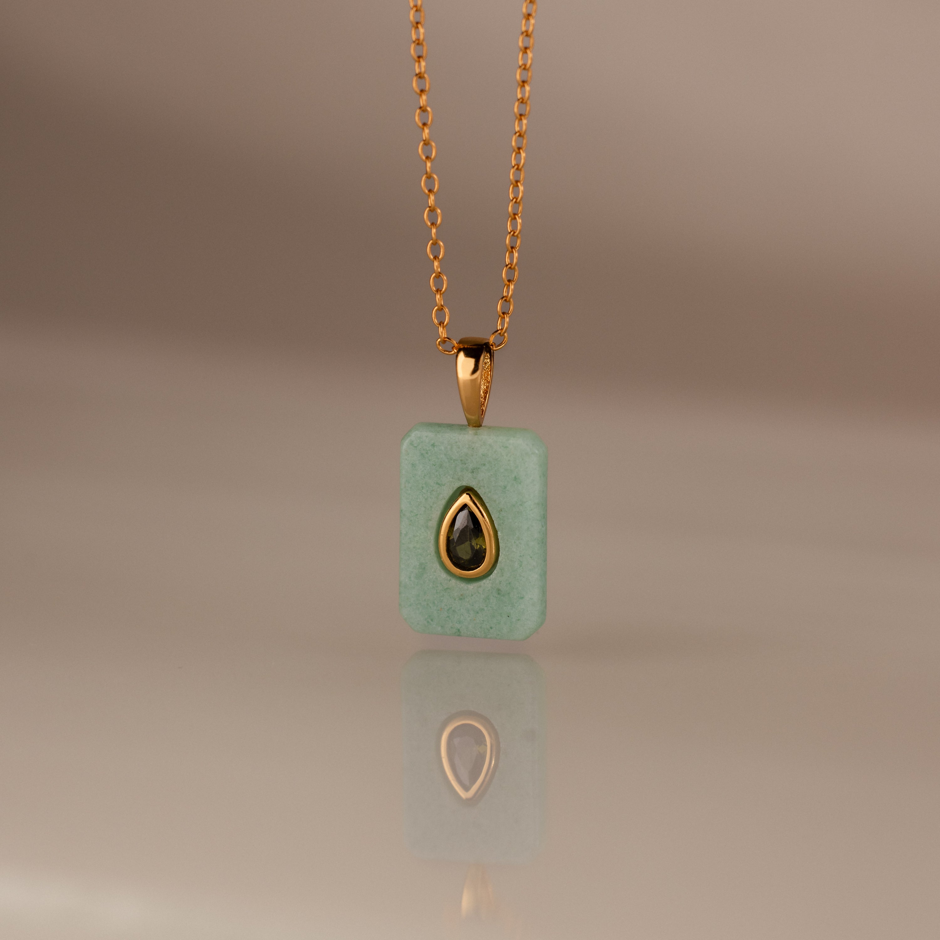 The Peridot Crystal Necklace features a rectangular green crystal pendant in a gold bezel setting, highlighted by a gold-trimmed teardrop accent at the center.
