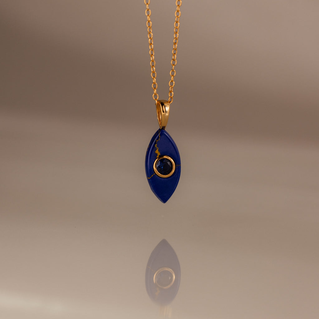 The Sapphire Crystal Necklace features a gold chain and a blue, marquise-shaped pendant with a gold spiral design, making it a perfect Birthstone Crystal Necklace for any occasion.
