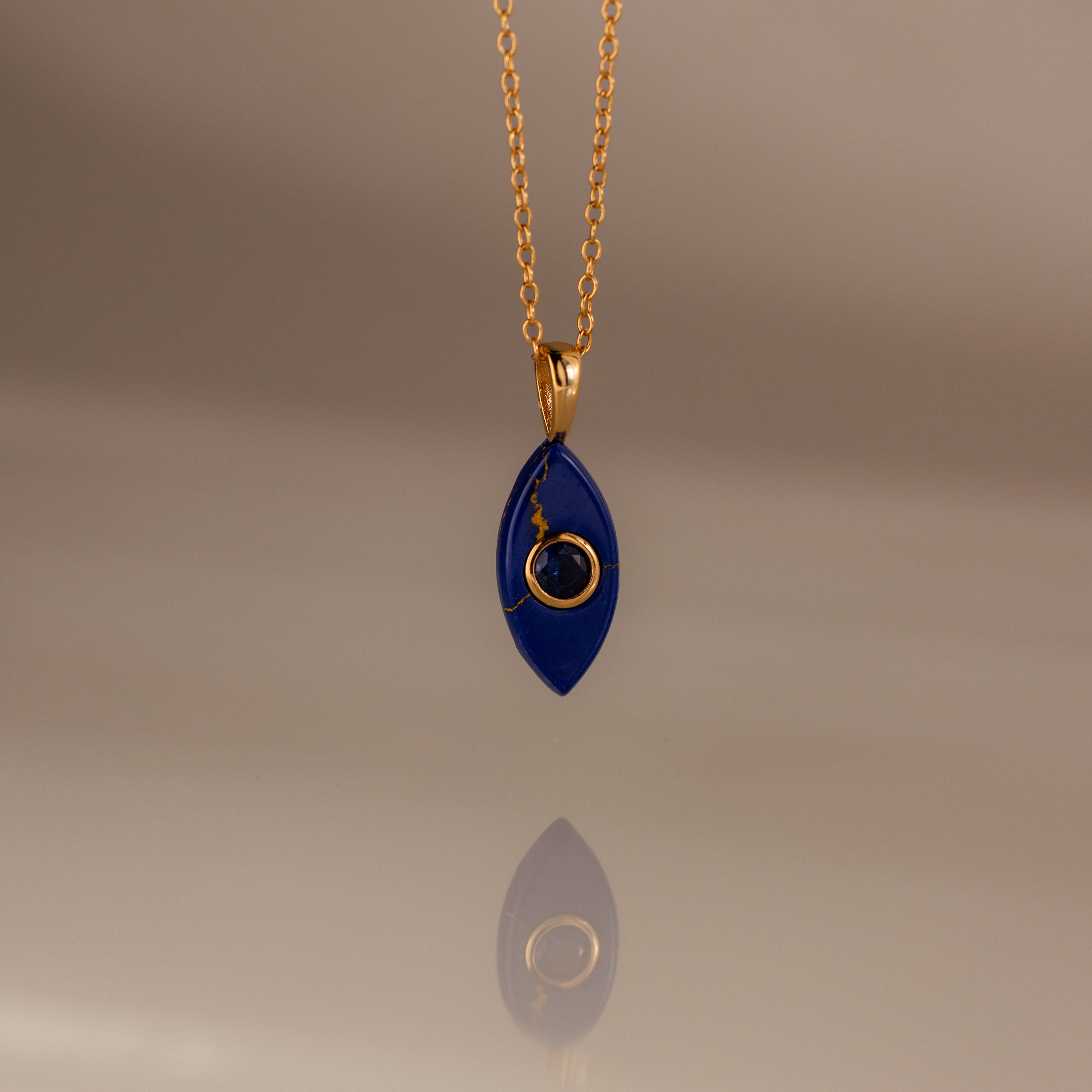 The Sapphire Crystal Necklace features a gold chain and a blue, marquise-shaped pendant with a gold spiral design, making it a perfect Birthstone Crystal Necklace for any occasion.