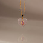 The Pink Tourmaline Crystal Necklace features a gold chain with a heart-shaped pendant, showcasing a bezel-set pink tourmaline birthstone at the center, displayed on a neutral background.
