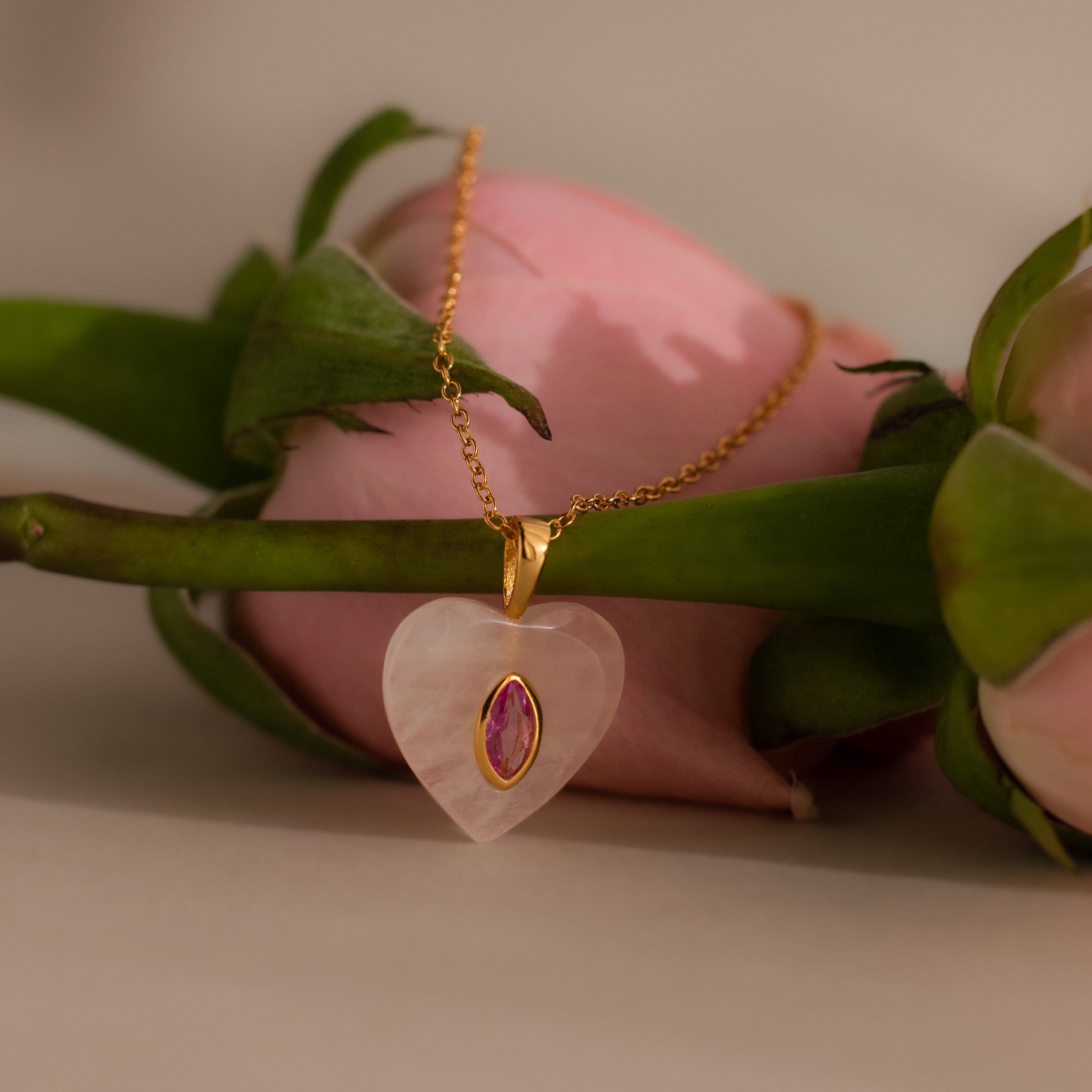A Pink Tourmaline Crystal Necklace with a heart-shaped pendant rests on a pink rose, radiating elegance and charm.