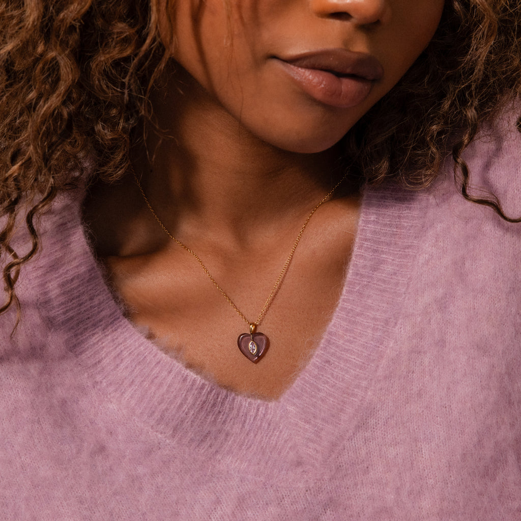 Woman wearing a lilac sweater and the Birthstone Crystal Necklace, featuring a gold chain with a purple heart-shaped birthstone crystal pendant.