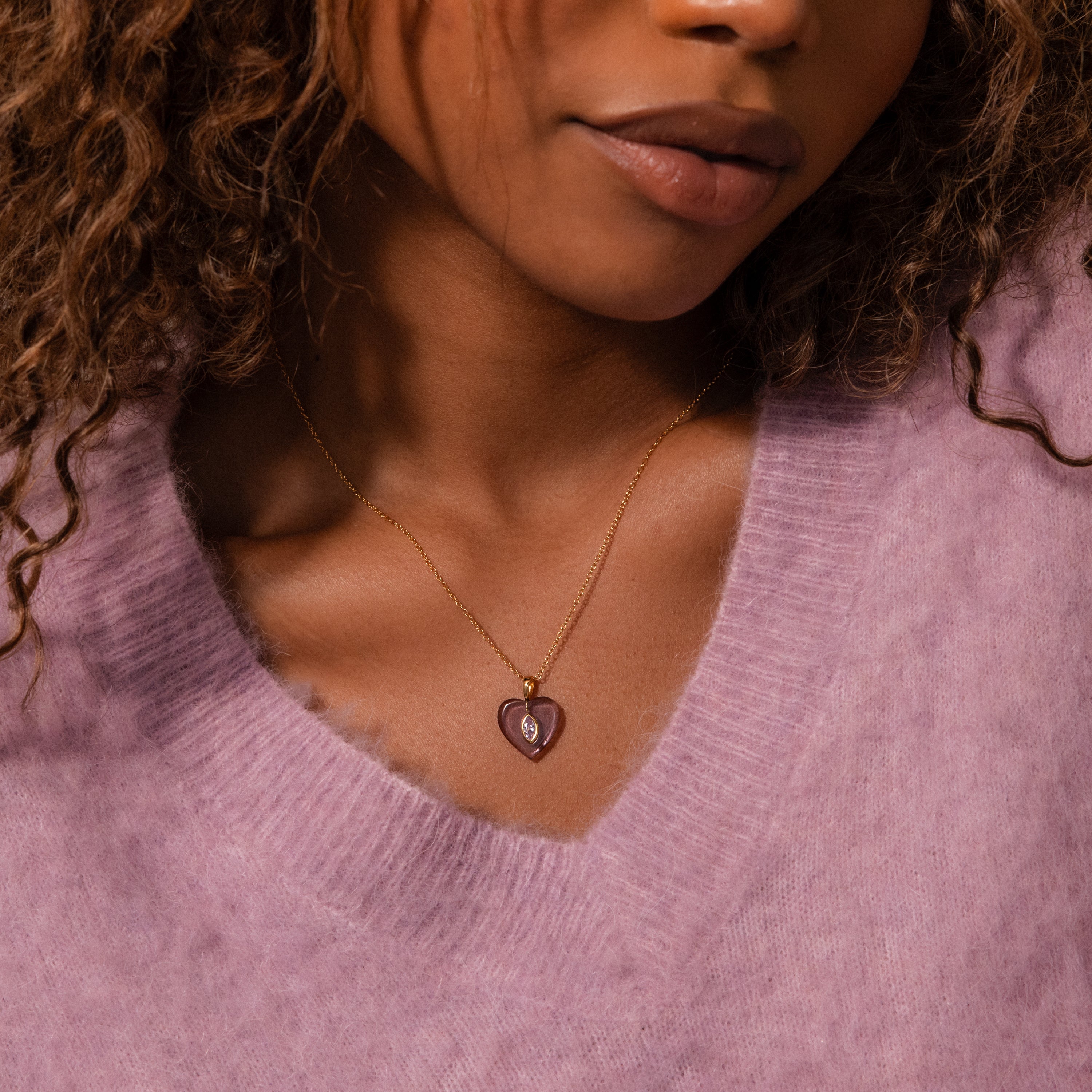 Woman wearing a lilac sweater and the Birthstone Crystal Necklace, featuring a gold chain with a purple heart-shaped birthstone crystal pendant.