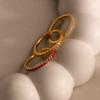 The Endless Eternity Birthstone Ring, along with two other gold gemstone rings, rests on a smooth, white, rounded surface.