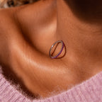 The Endless Eternity Birthstone Ring with pink stones rests elegantly on a woman's collarbone, casting a delicate shadow on her skin.