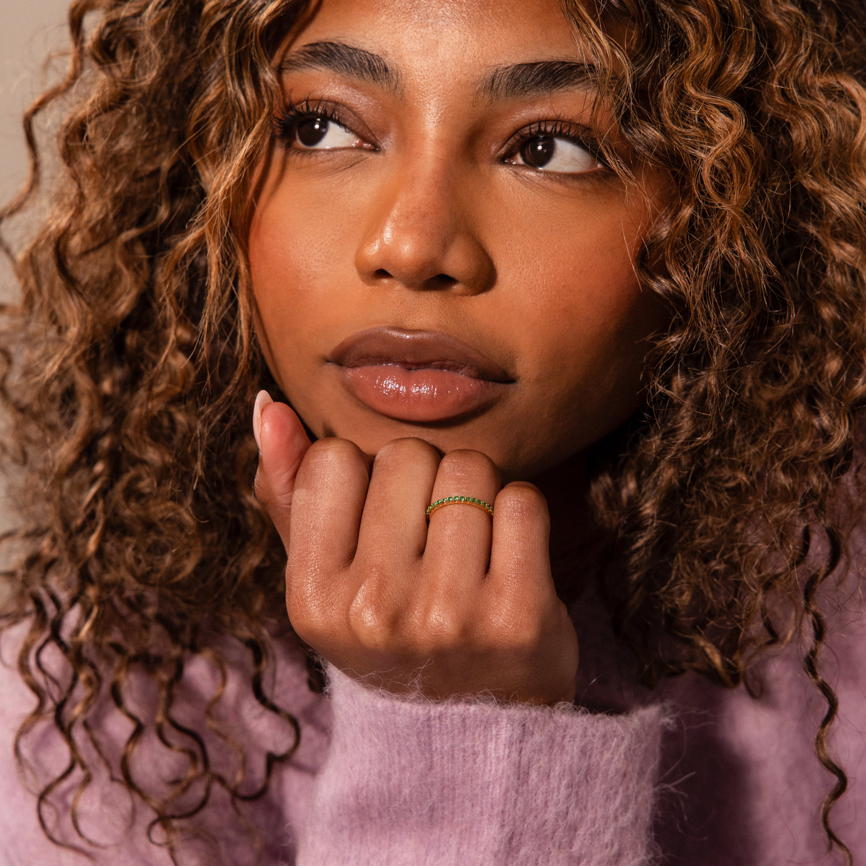 A woman with curly hair in a purple sweater with lace accents rests her chin on her hand, displaying the Lace Eternity Garnet Ring.