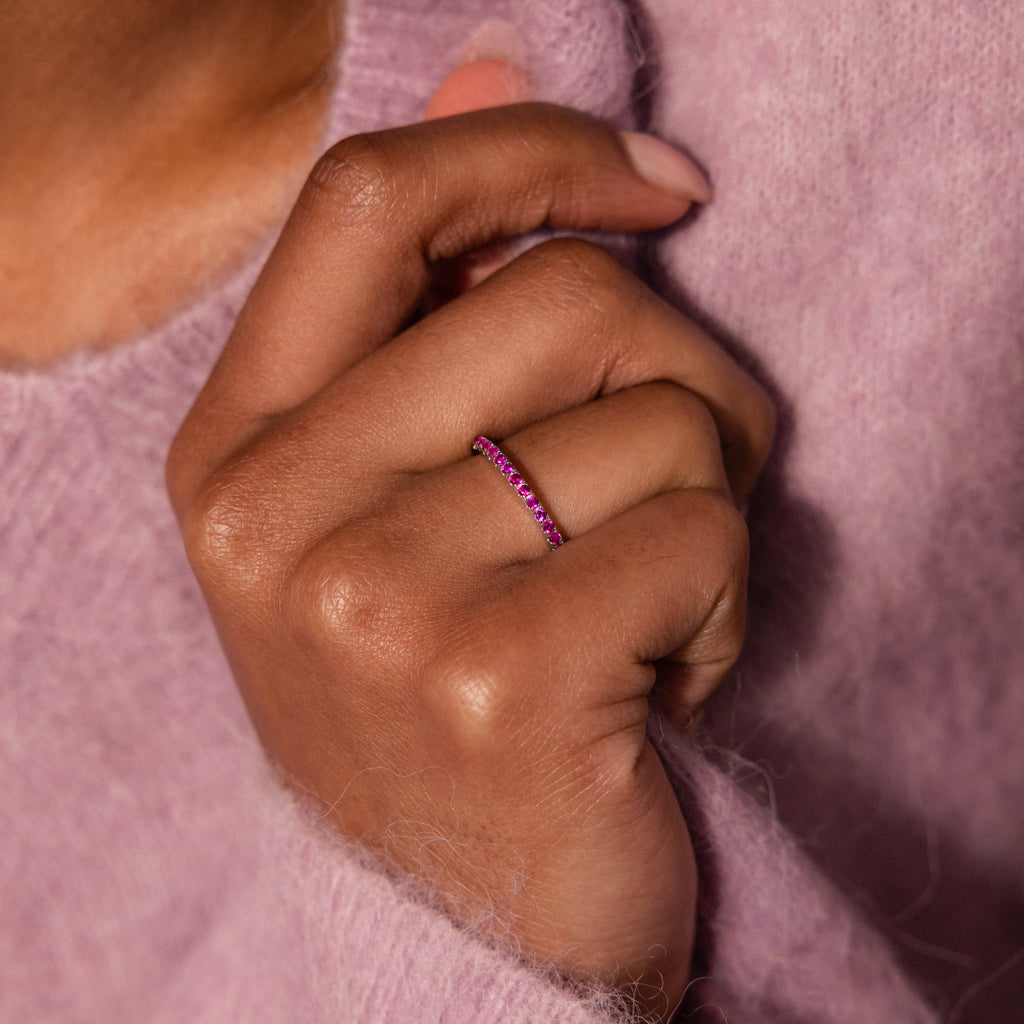 A hand wearing the Lace Eternity Garnet Ring, with a mauve fuzzy sweater in the background.