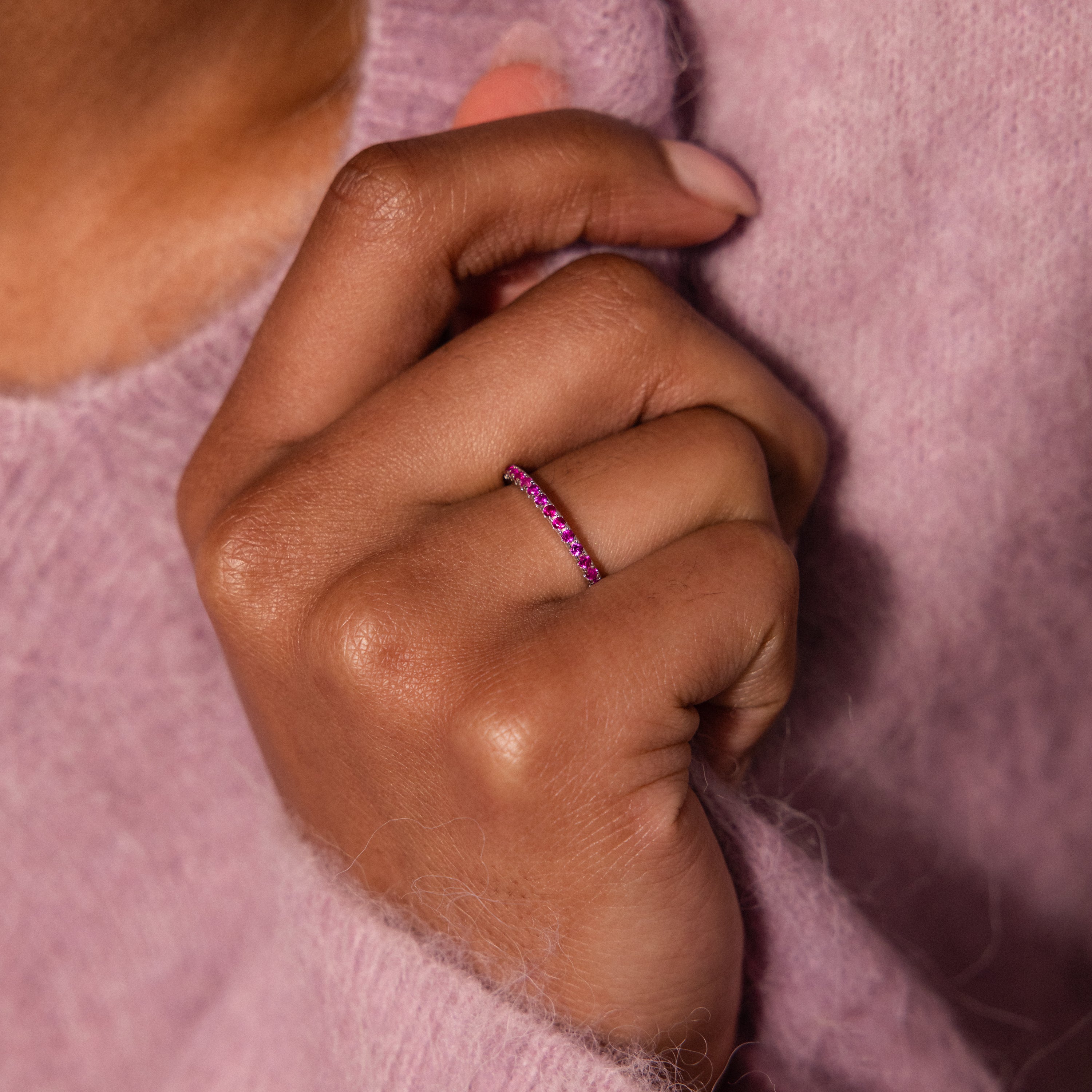 A hand adorned with the Endless Eternity Ruby Ring, featuring elegant pink gemstones, with a fuzzy pink sweater in the background.