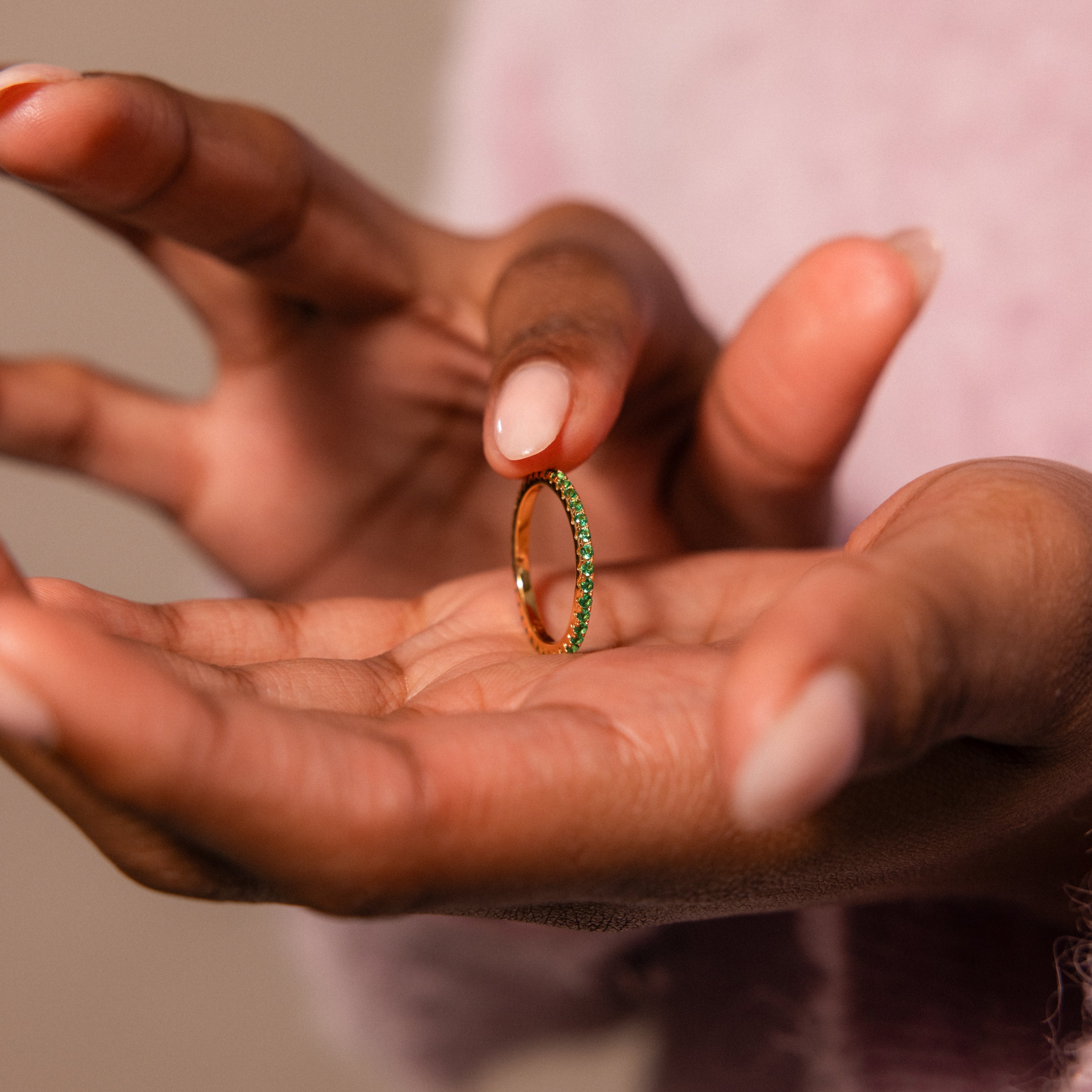 A person holds an elegant Endless Eternity Topaz Ring featuring green stones between their thumb and forefinger.