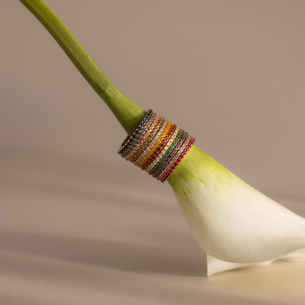 The Endless Eternity Birthstone Rings are stacked on the stem of a white calla lily, showcasing their vibrant colors and timeless elegance.