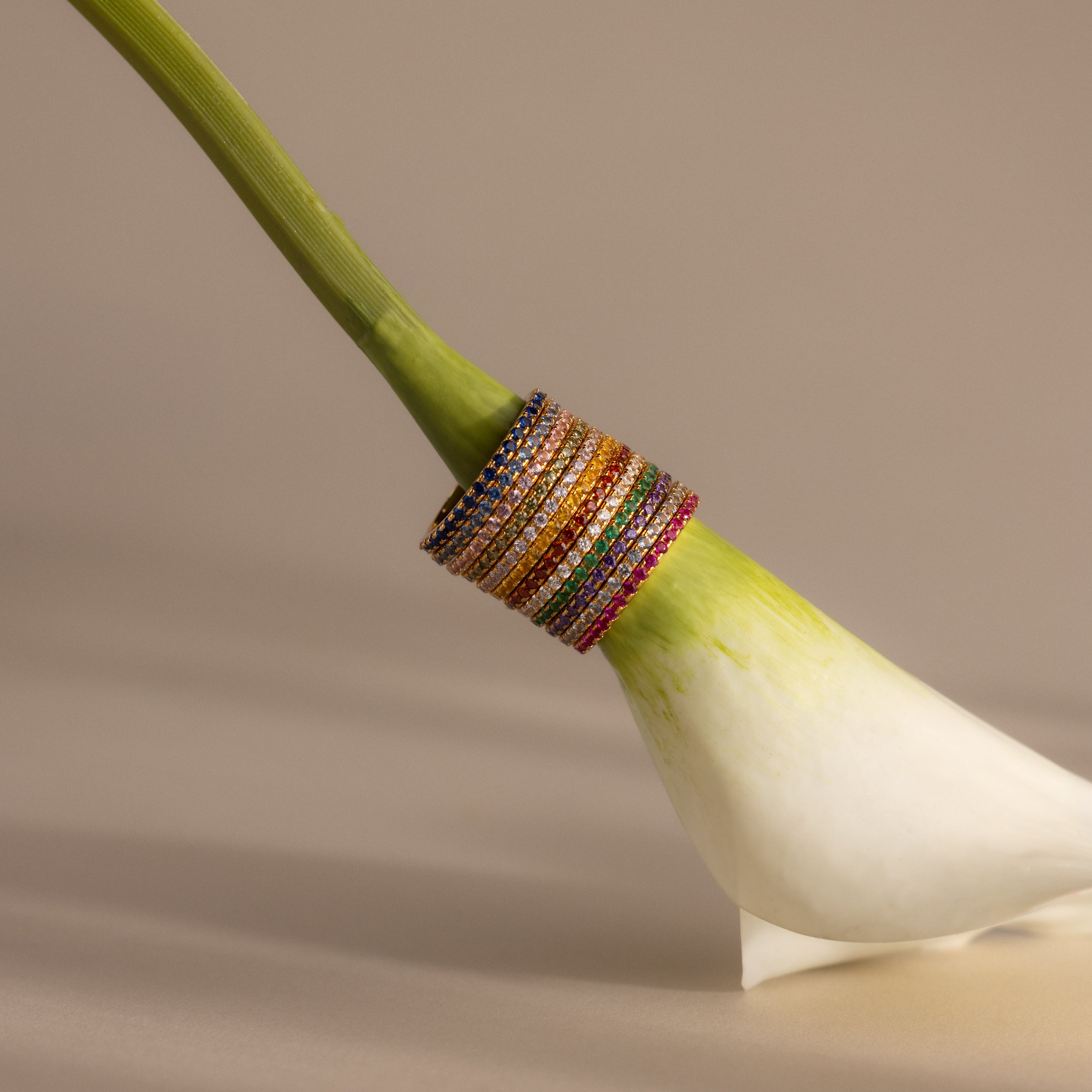 The Endless Eternity Birthstone Rings are stacked on the stem of a white calla lily, showcasing their vibrant colors and timeless elegance.