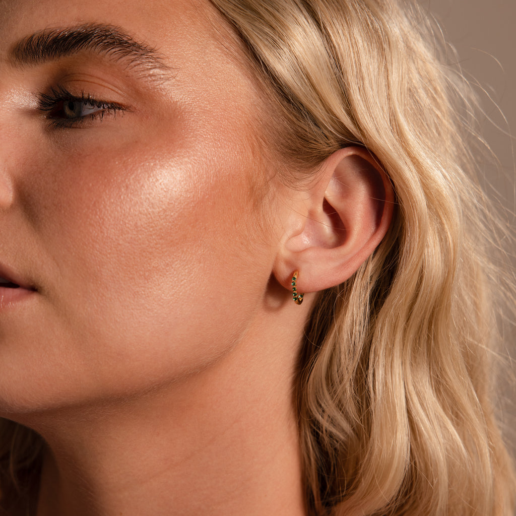 Close-up of a woman with wavy blonde hair wearing the Inside Out Sapphire Huggies, a small gold stacking earring, in her left ear.