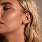 Close-up of a woman with wavy blonde hair wearing the Inside Out Sapphire Huggies, a small gold stacking earring, in her left ear.