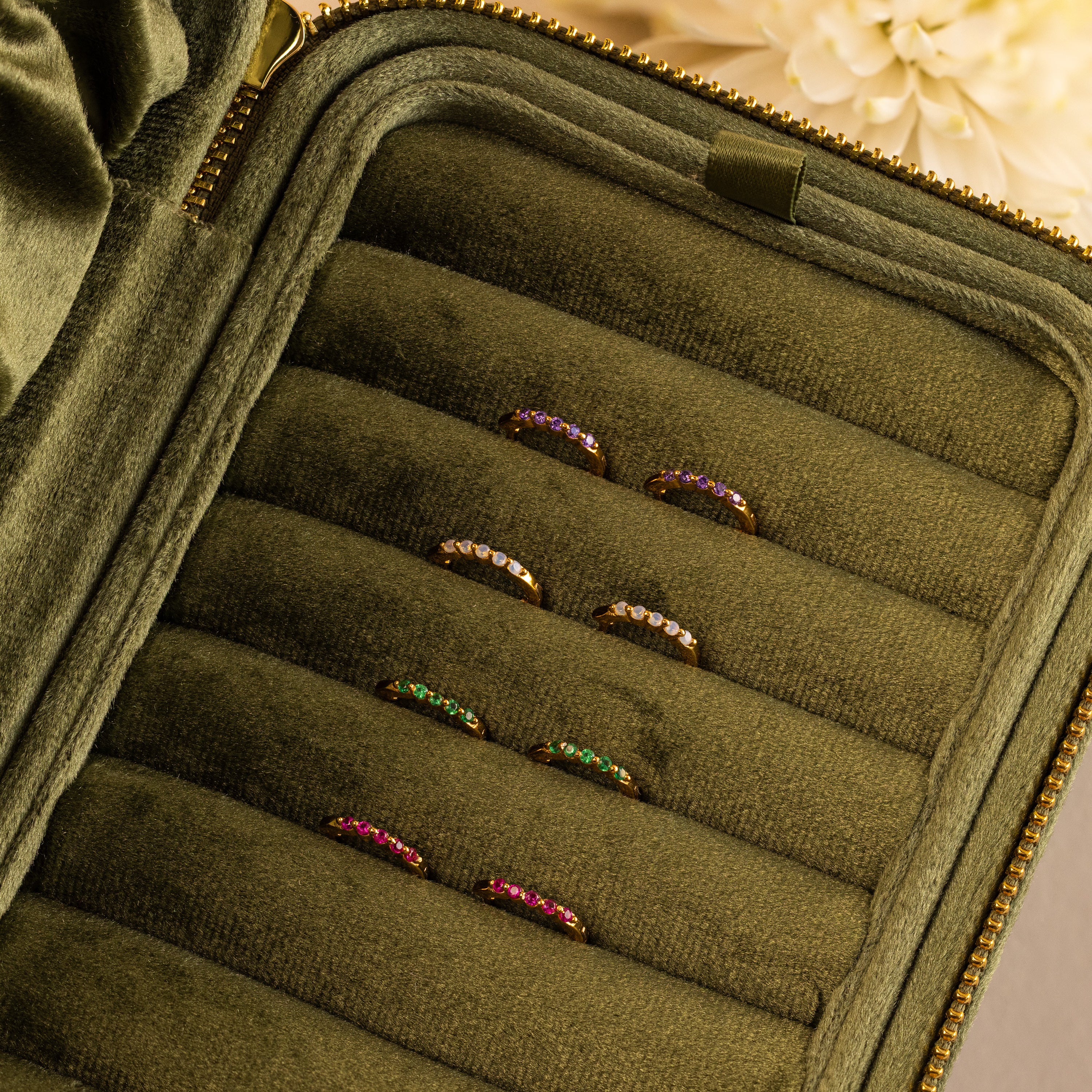 Seven colorful gemstone rings are neatly arranged in a green velvet zippered ring case, making it perfect for pairing with your favorite stacking earrings or Inside Out Ruby Huggies.