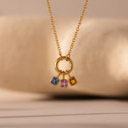 The Square Bezel Sapphire Charm features three square gemstones—blue, pink, and yellow—set in gold on a circular pendant. This elegant gold necklace is a stunning piece of gemstone jewelry, perfect for any occasion.