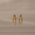 Amelia Duo Diamond Huggies – gold V-shaped modern earrings featuring sparkling diamonds, showcased on a reflective beige surface.