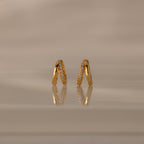 Amelia Duo Diamond Huggies – gold V-shaped modern earrings featuring sparkling diamonds, showcased on a reflective beige surface.