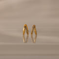Amelia Duo Birthstone Huggies in Aquamarine (March), gold V-shaped modern earrings with small gemstones, displayed on a reflective beige surface.