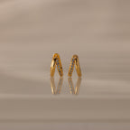 Amelia Duo Birthstone Huggies in Aquamarine (March), gold V-shaped modern earrings with small gemstones, displayed on a reflective beige surface.