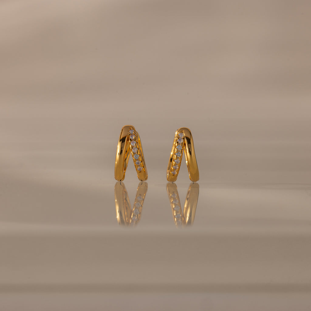 Amelia Duo Opal Huggies—gold hoop earrings with opal accents—are styled as modern huggies and displayed on a reflective beige surface.