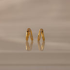 Amelia Duo Opal Huggies—gold hoop earrings with opal accents—are styled as modern huggies and displayed on a reflective beige surface.
